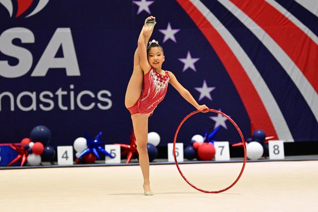 A gymnast rolling the hoop along the floor during a routine